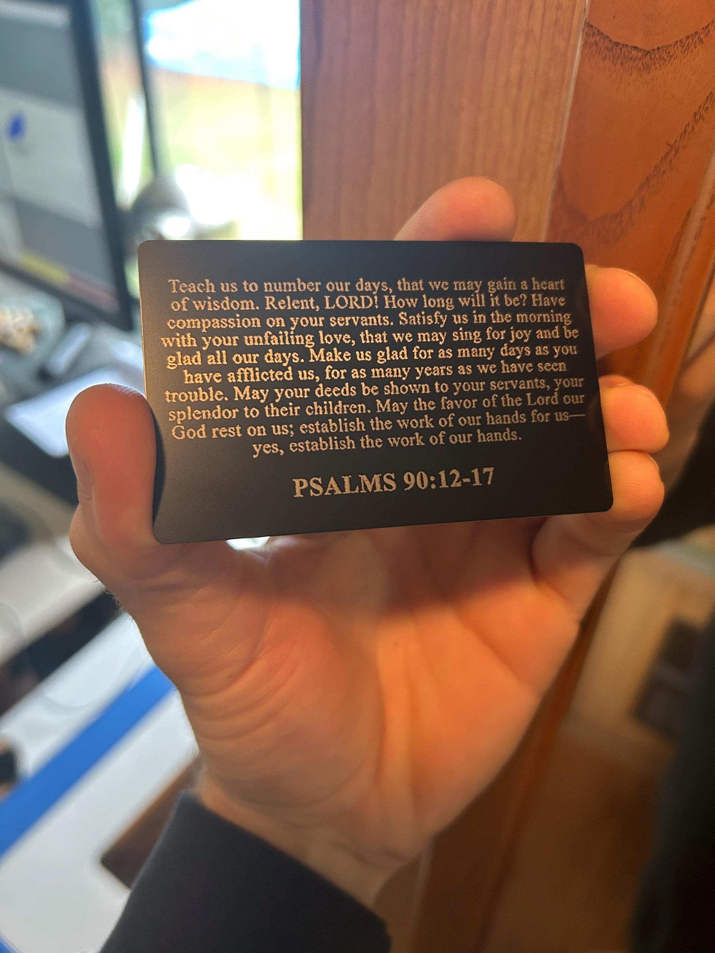 Hand holding a metal bible bookmark card with Psalms 90:12-17 text, blurred background