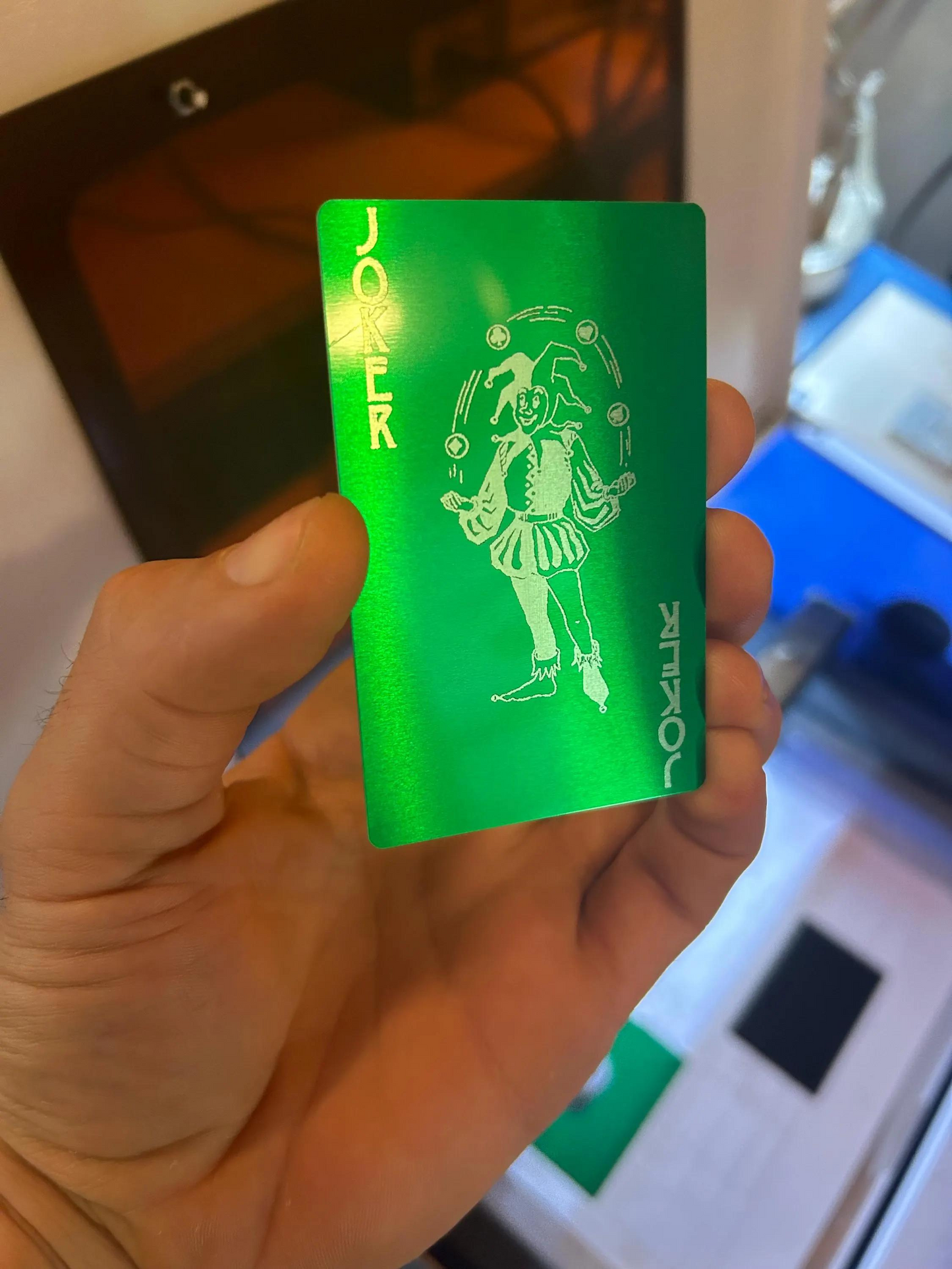 Green card with a jester design held by a hand, with a blurred background
