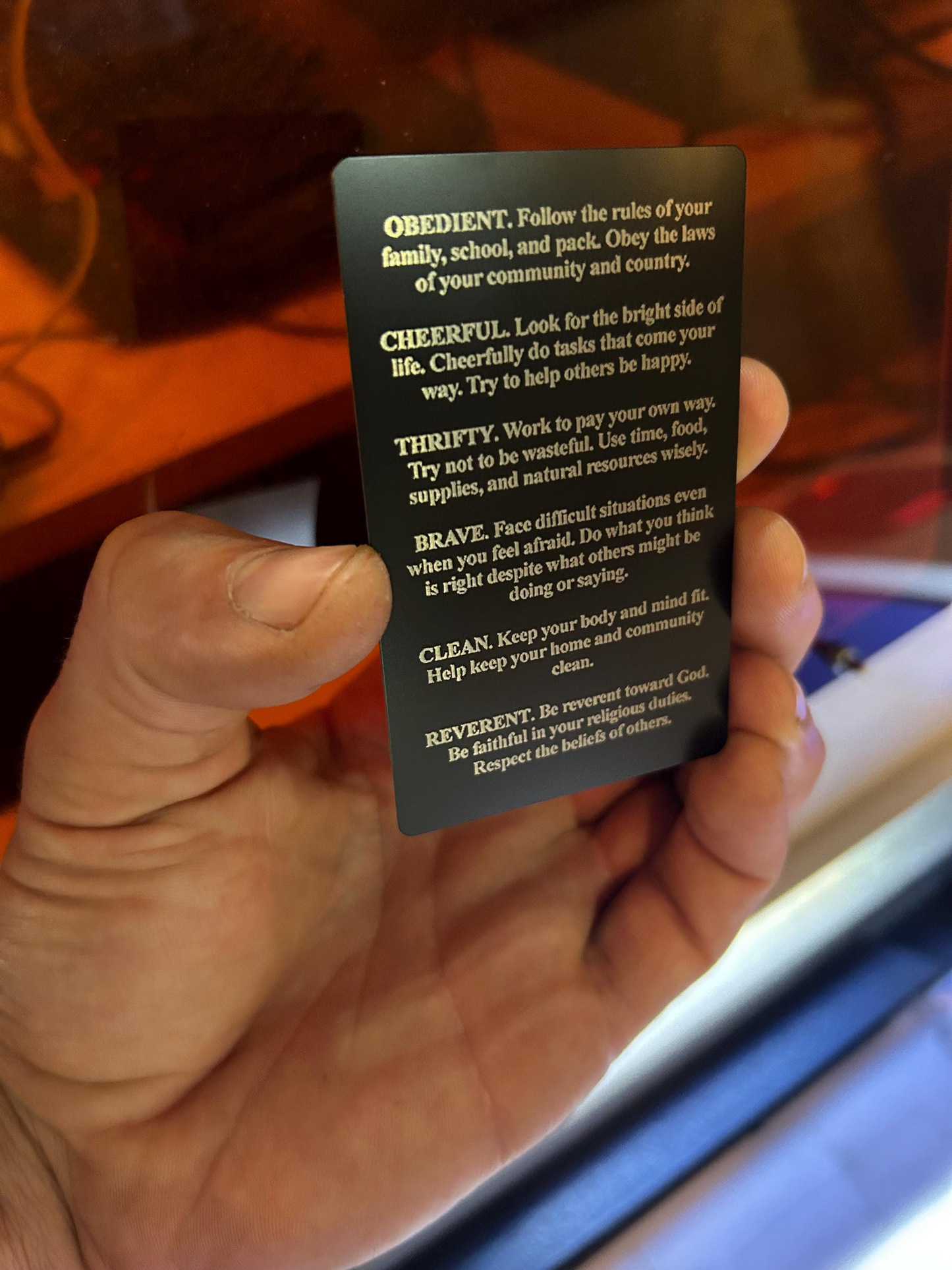Hand holding a black card with 12 points of scout law, reverse side on a blurred background