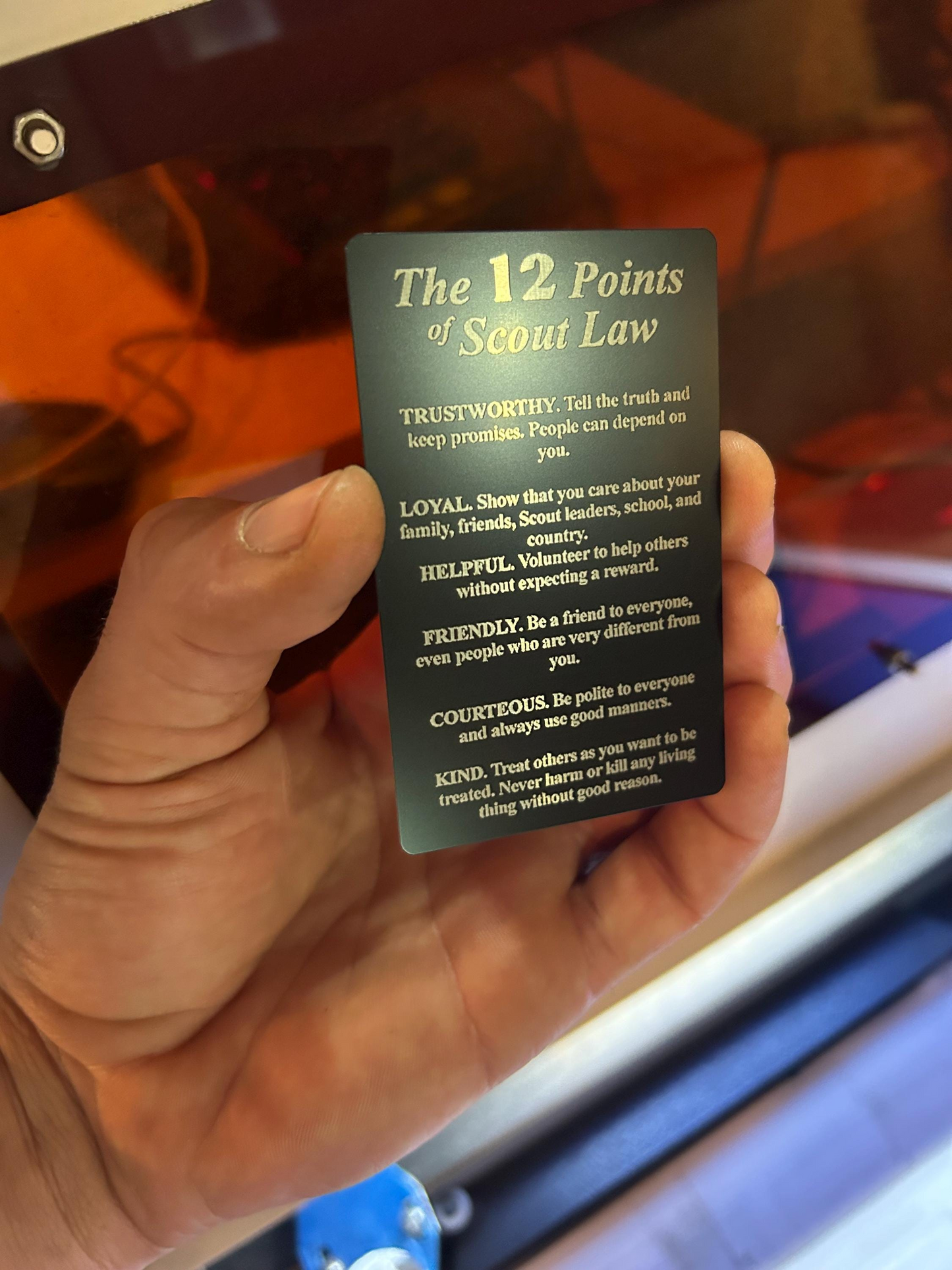 Hand holding a metal keepsake card with 'The 12 Points of Scout Law' engraved on anodized aluminum