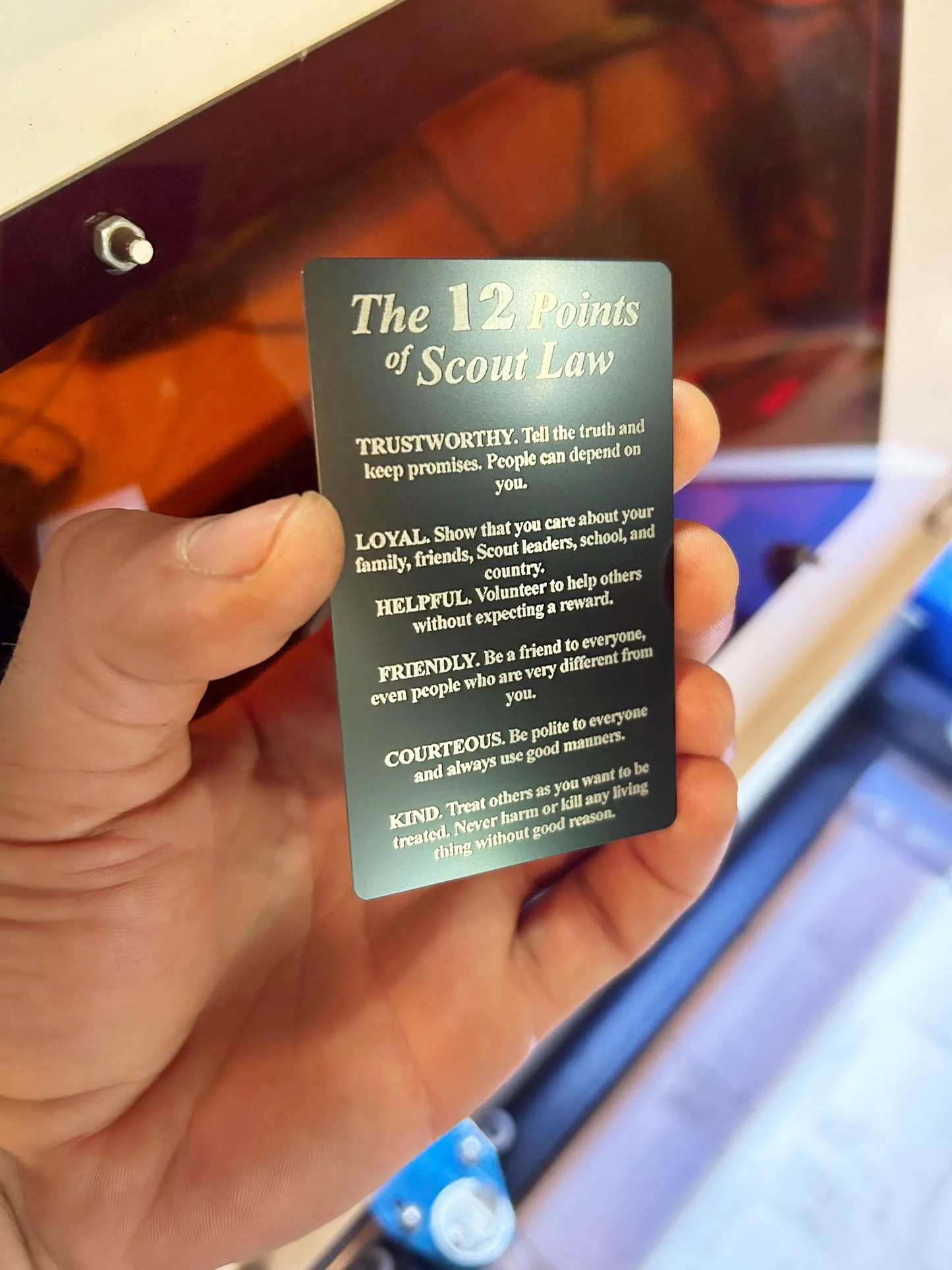 Hand holding a metal laser engraved wallet insert with 'The 12 Points of Scout Law' text.
