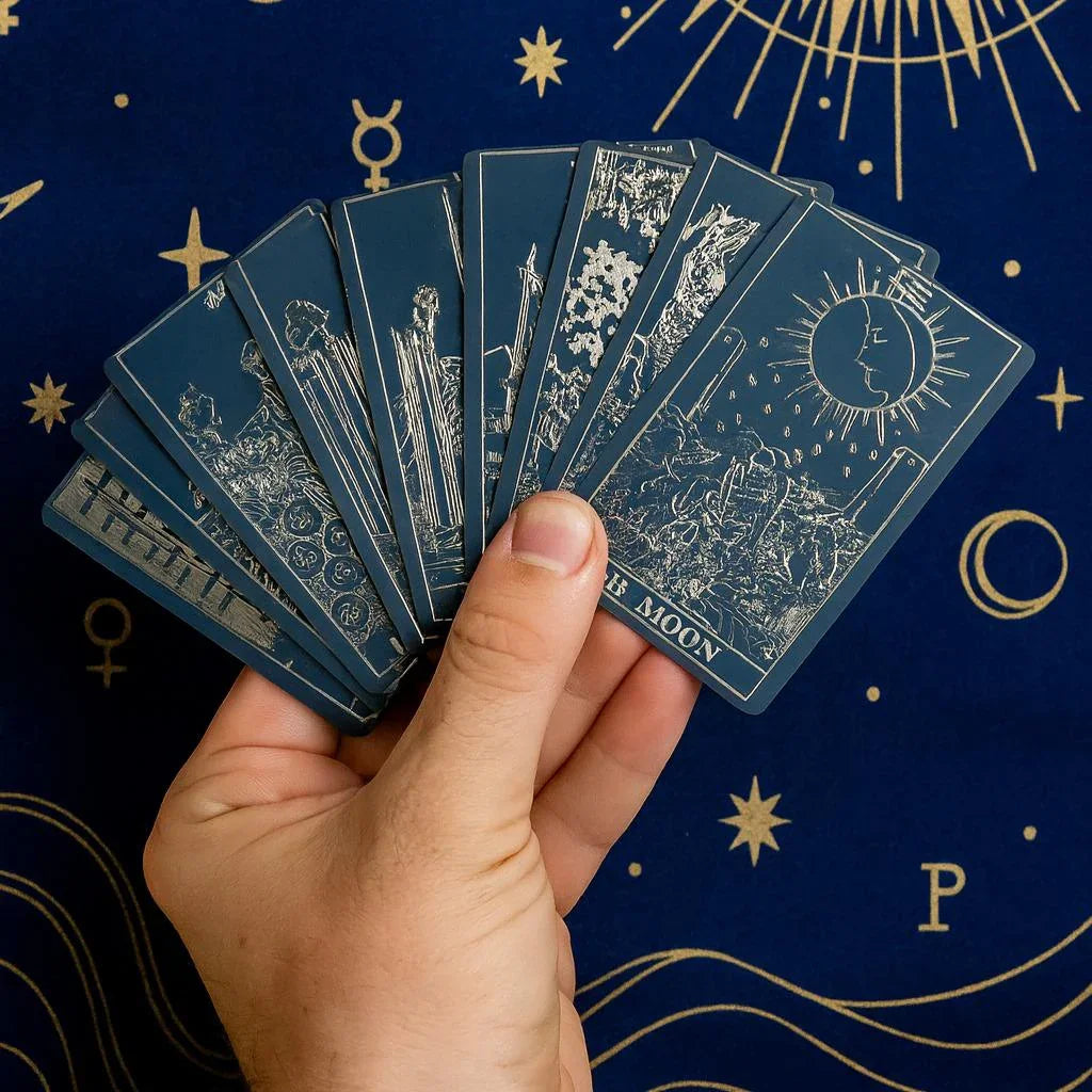 Hand holding tarot cards against a dark blue background with star and moon symbols