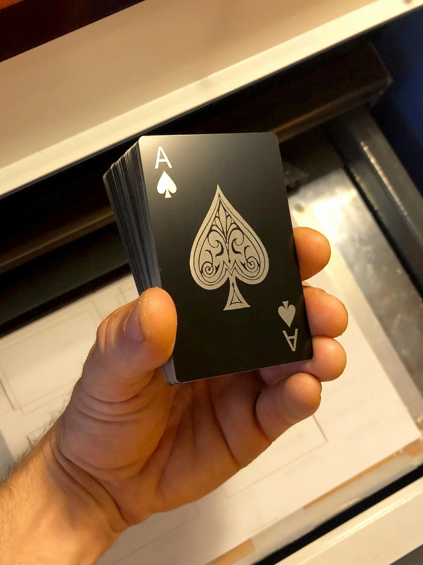 Hand holding a deck of metal matte black/silver laser engraved playing cards with an ace of spades on a neutral background
