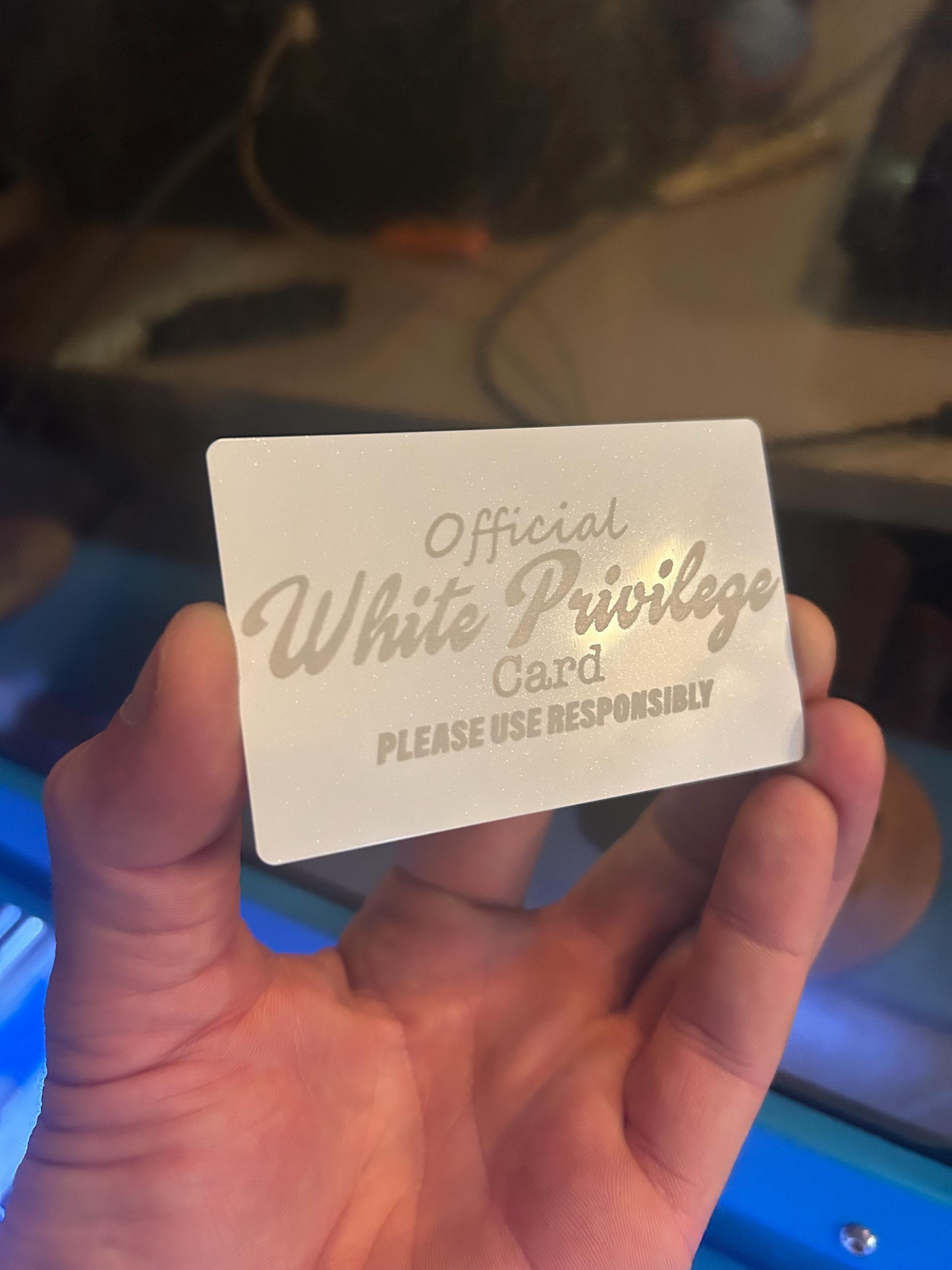 Hand holding a white/silver metal gift card with 'Official White Privilege Card' text.