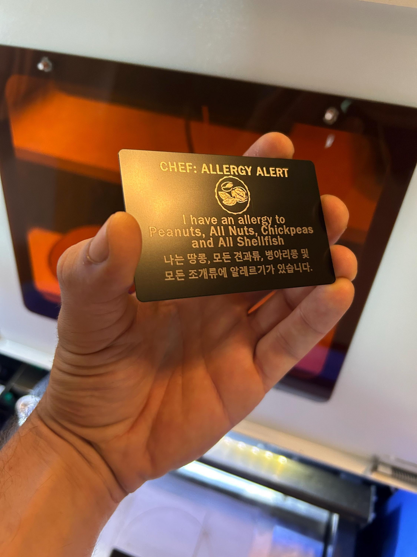 Hand holding a metal food allergy alert card with custom text engraving.