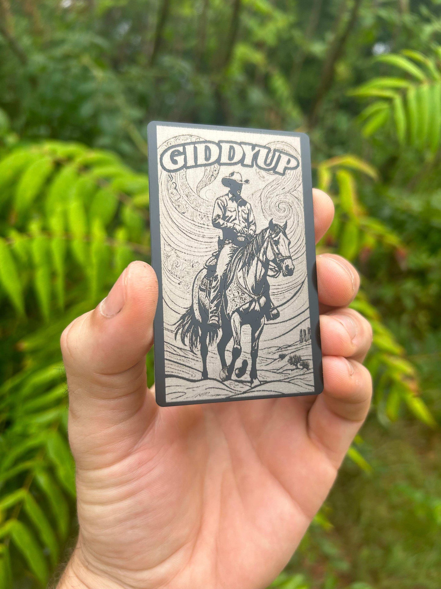Hand holding a small rectangular wallet insert with a western cowboy design and 'Giddy Up' text against a green background.