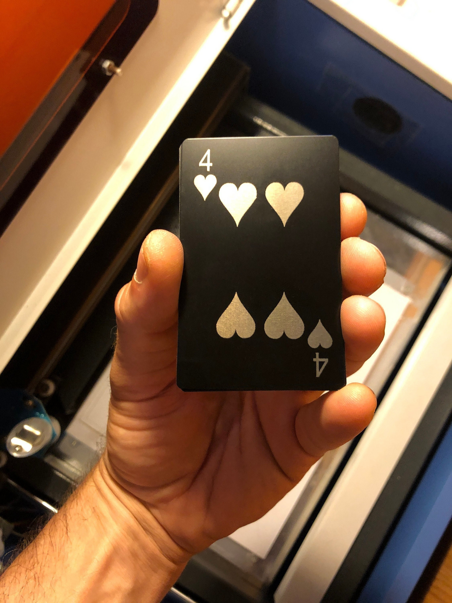 Hand holding a metal Four of Hearts laser engraved anodized aluminum playing card with four hearts design