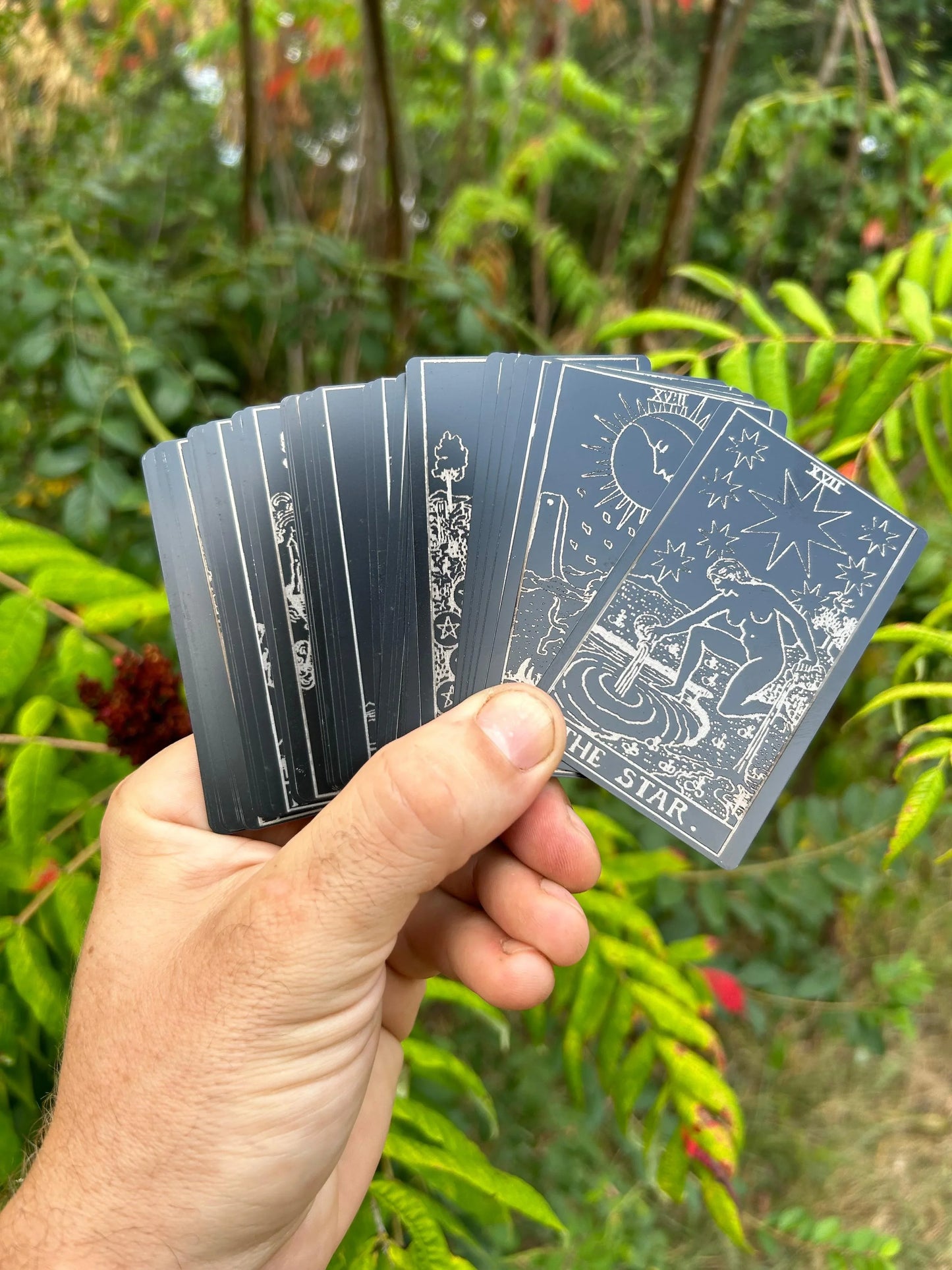 Hand holding a complete deck of laser engrave metal tarot cards with a natural background