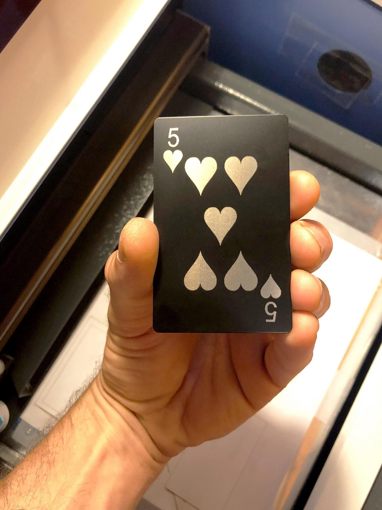 Hand holding a metal poker gaming gift card with laser engraved five of hearts design in anodized aluminum