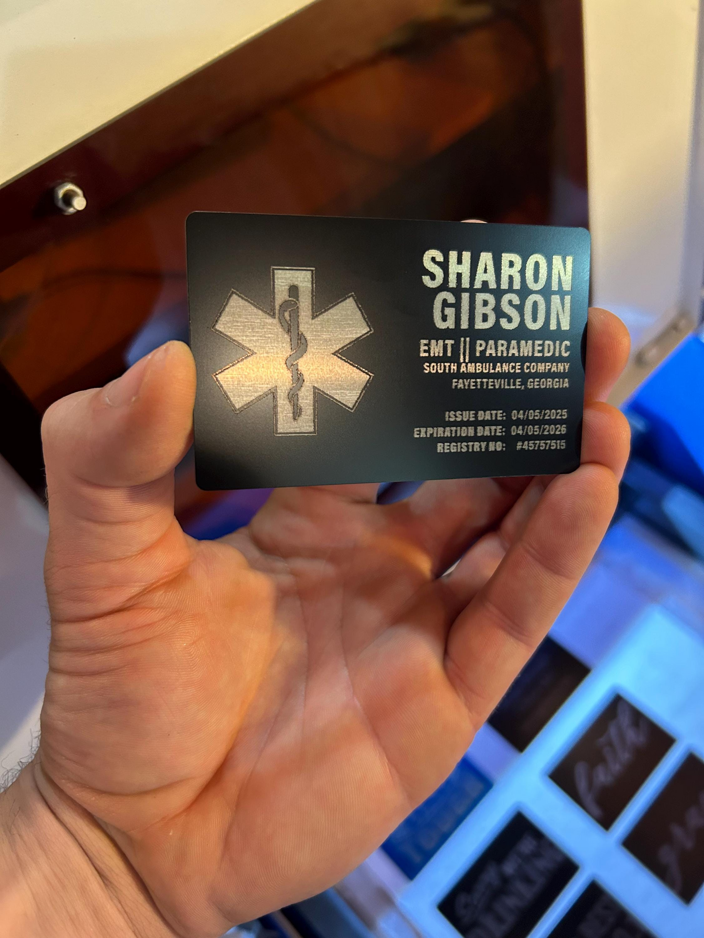Hand holding a personalized metal business card with medical emergency services details.