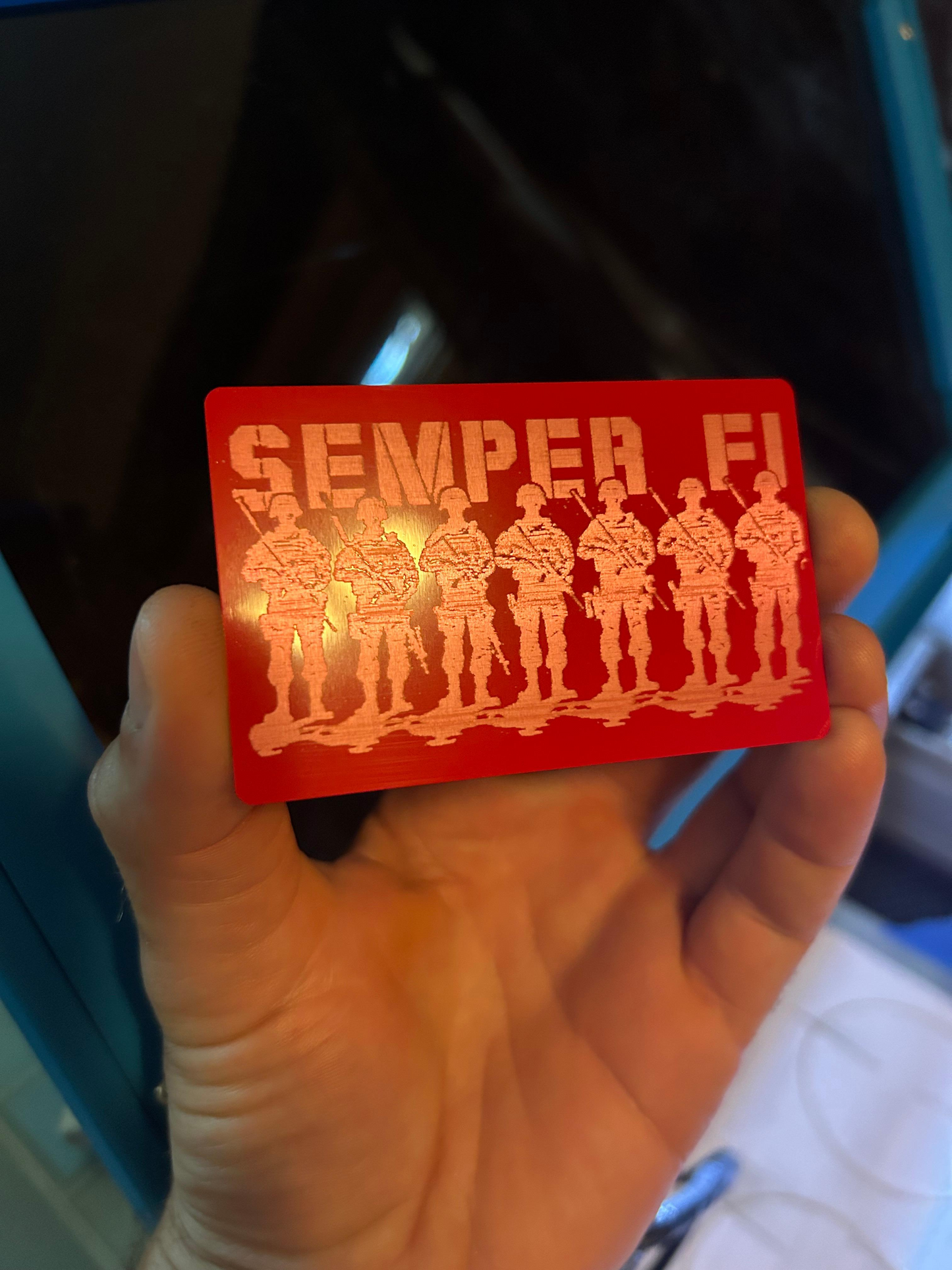 Metal Red/silver card with soldiers and 'Semper Fi' text held in a hand.