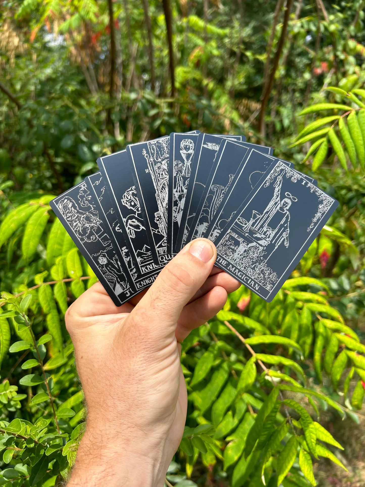 hand holding laser engraved metal tarot cards, with the magician card on top against a nature background