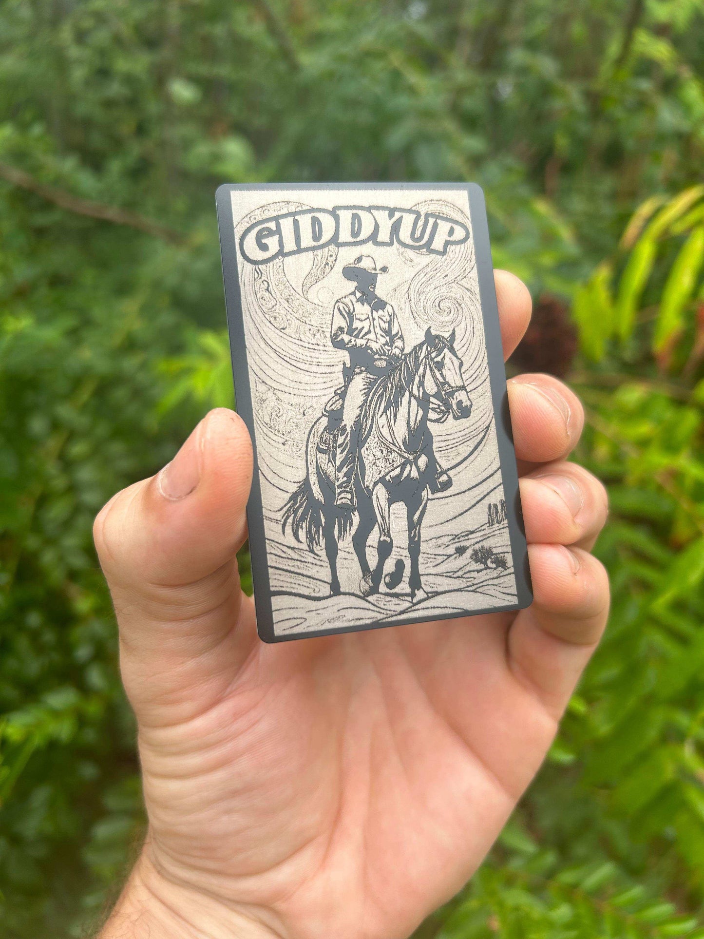Hand holding a small rectangular object with 'GIDDY UP' and a Wild West design against a green background.