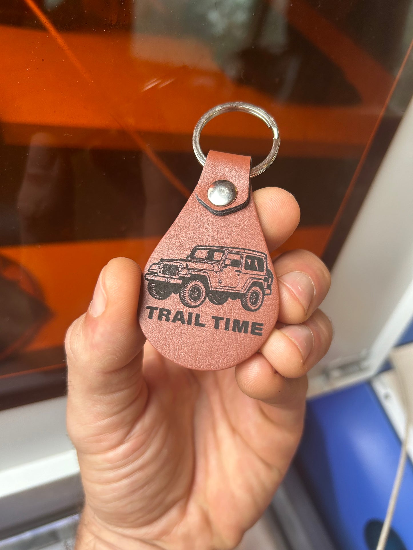 Hand holding a brown leather keychain with 'Trail Time' personalized engraving in front of a vehicle.