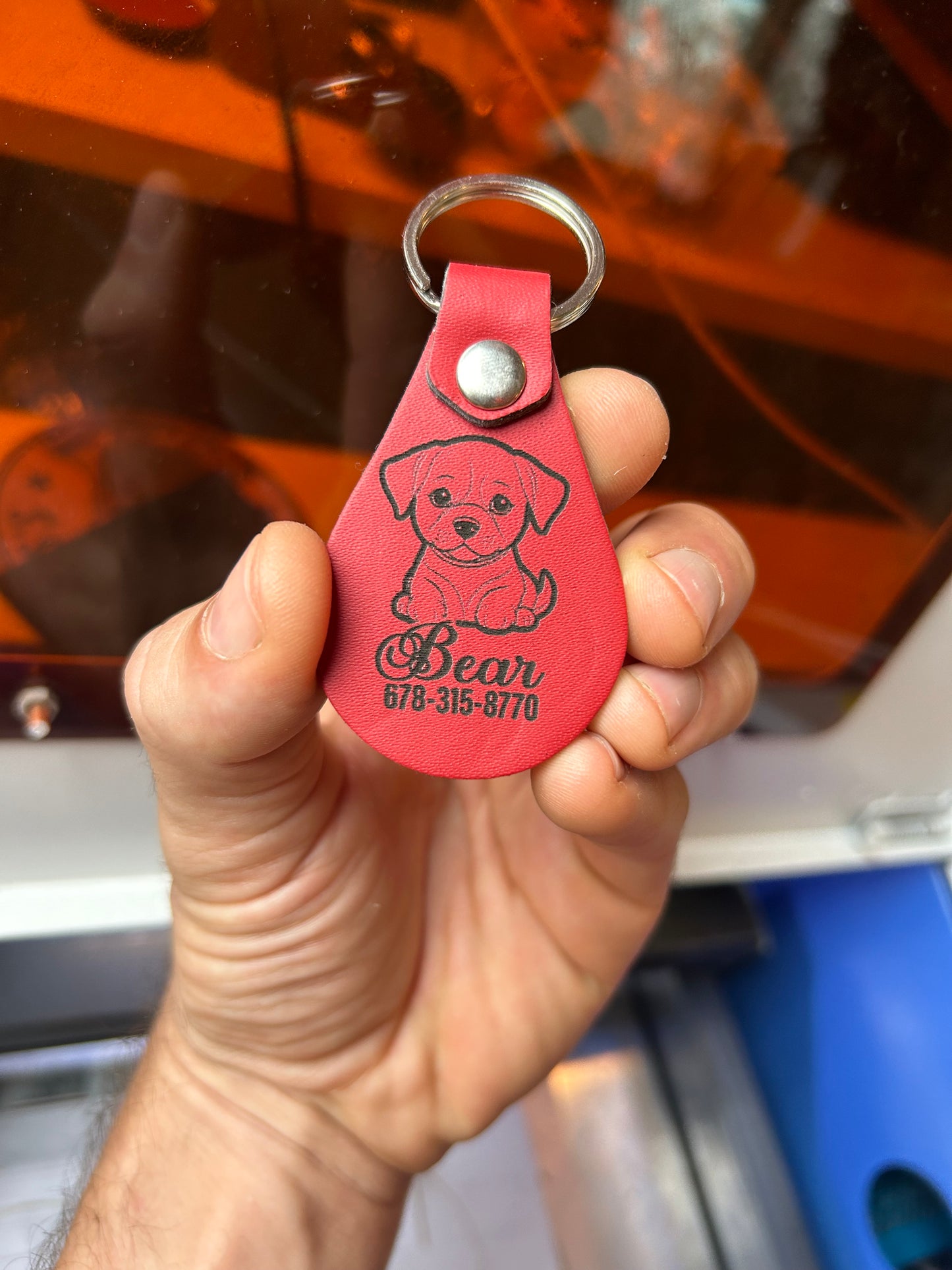 Hand holding a burgundy leather keychain with a puppy design and contact information engraving