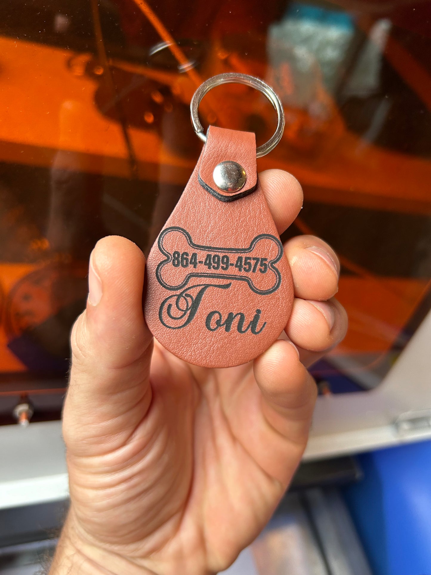 Hand holding laser engraved leather key fob with pet name and number in light brown
