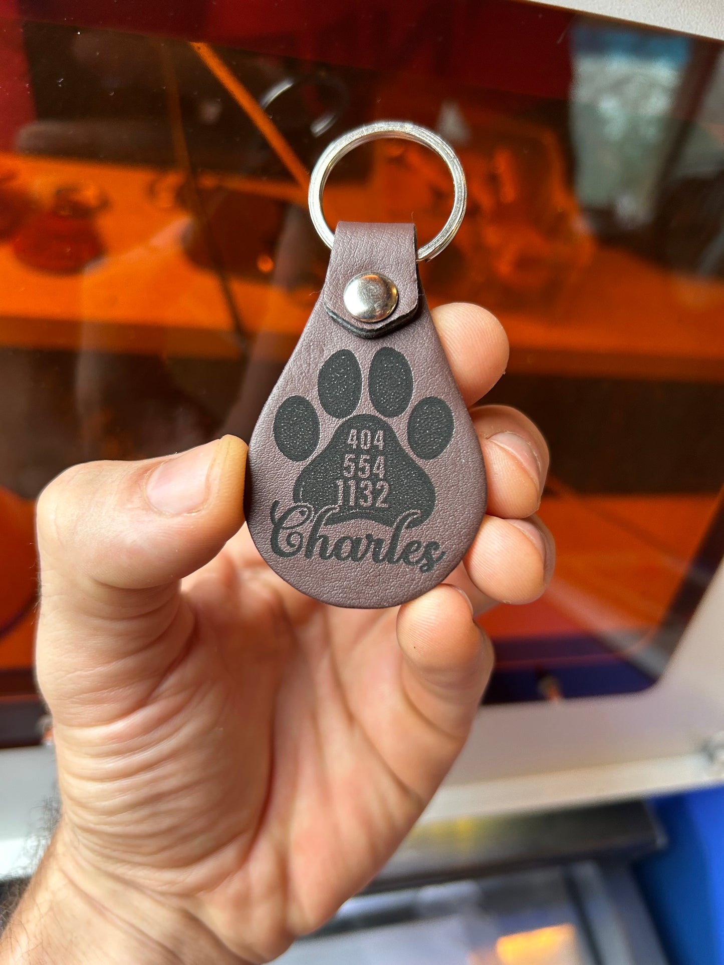 Hand holding a dark brown leather keychain with paw print design and pet name engraved text.