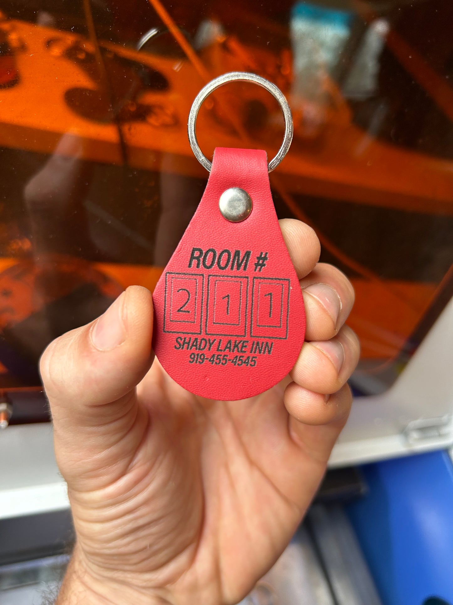 Hand holding a red key tag with room number laser engraving against a blurred background