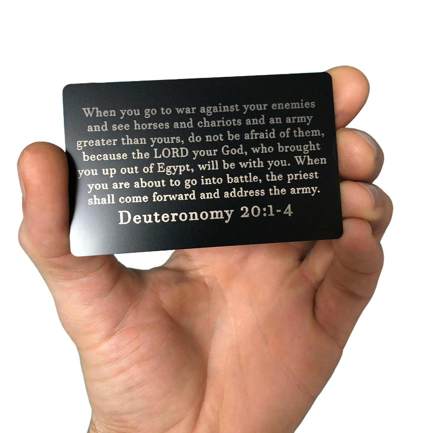 Hand holding a black card with text from Deuteronomy 20:1-4 against a white background