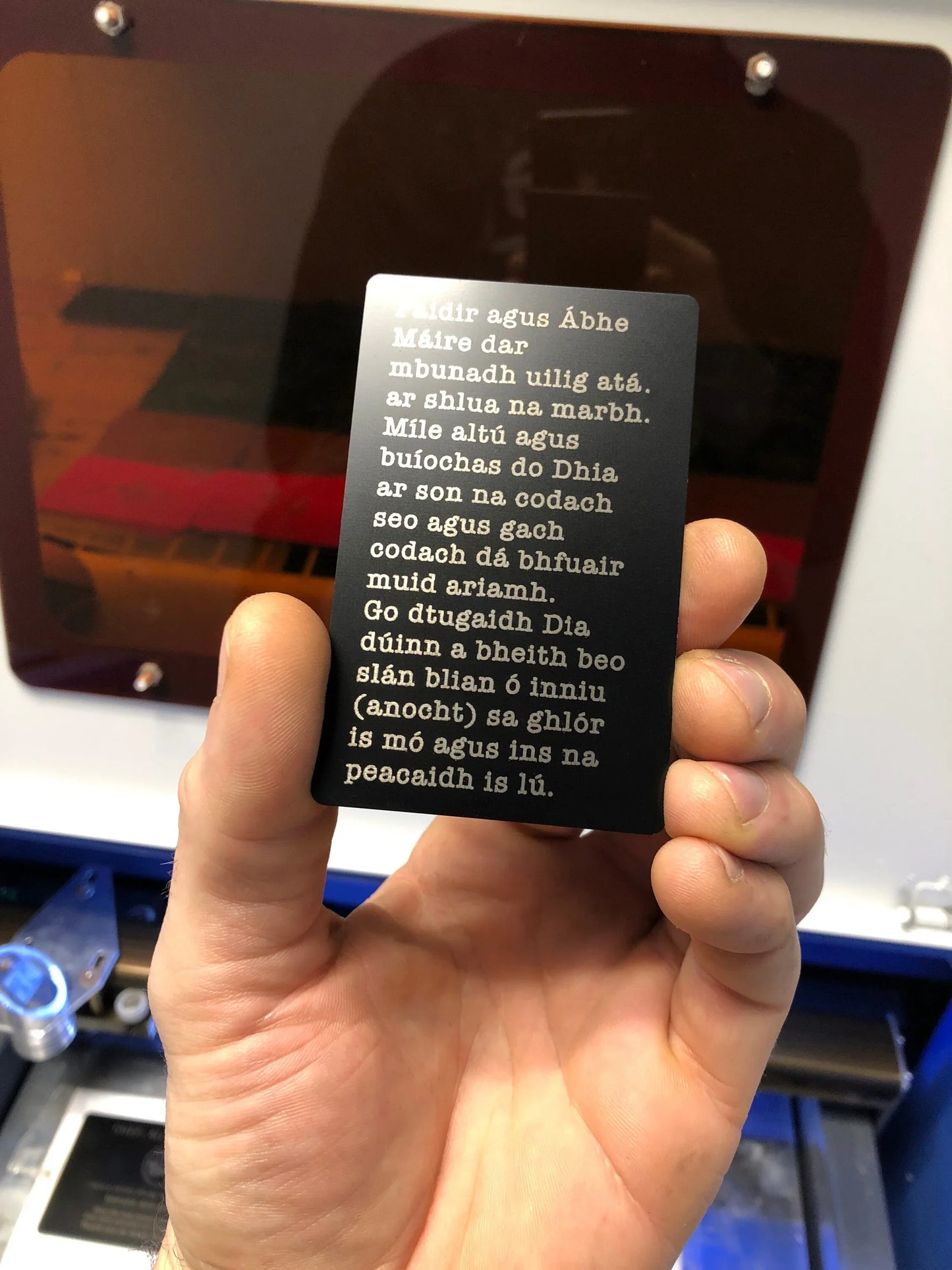 Hand holding a black engraved custom prayer card with white text against a blurred background