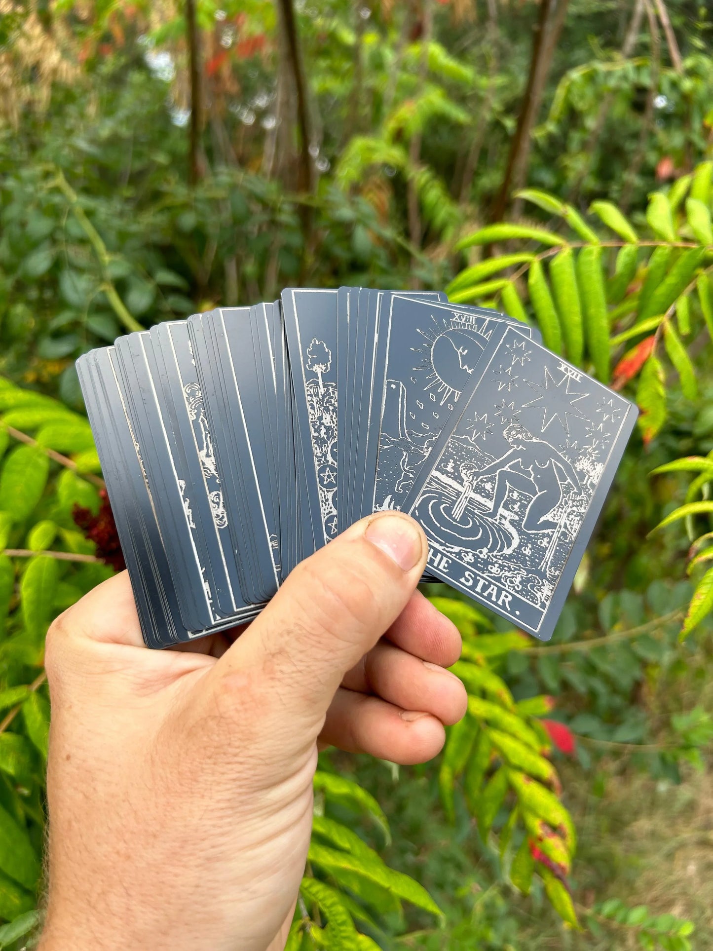 Hand holding a deck of metal tarot cards in matte/black silver with a natural background