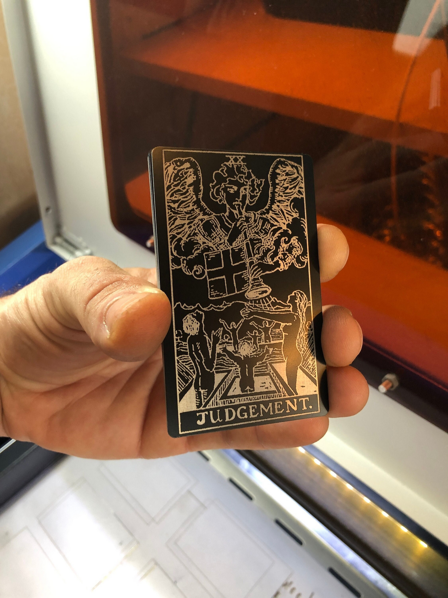 Hand holding a metal tarot card with 'Judgment' at the bottom, against a reflective surface.