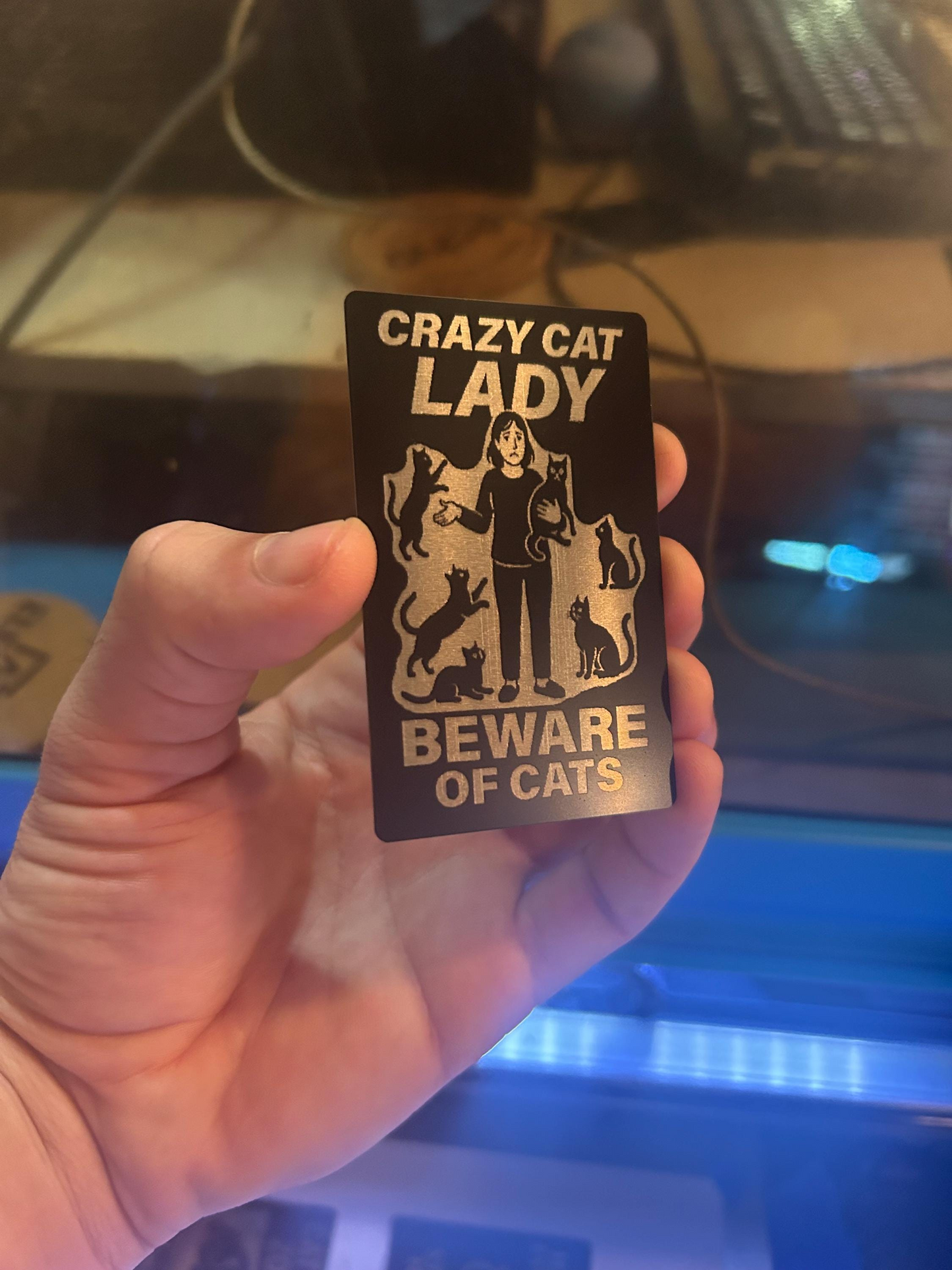 Angled shot of custom engraved metal gag gift card in black/silver with “Beware of Cats” design and CRAZY CAT LADY text