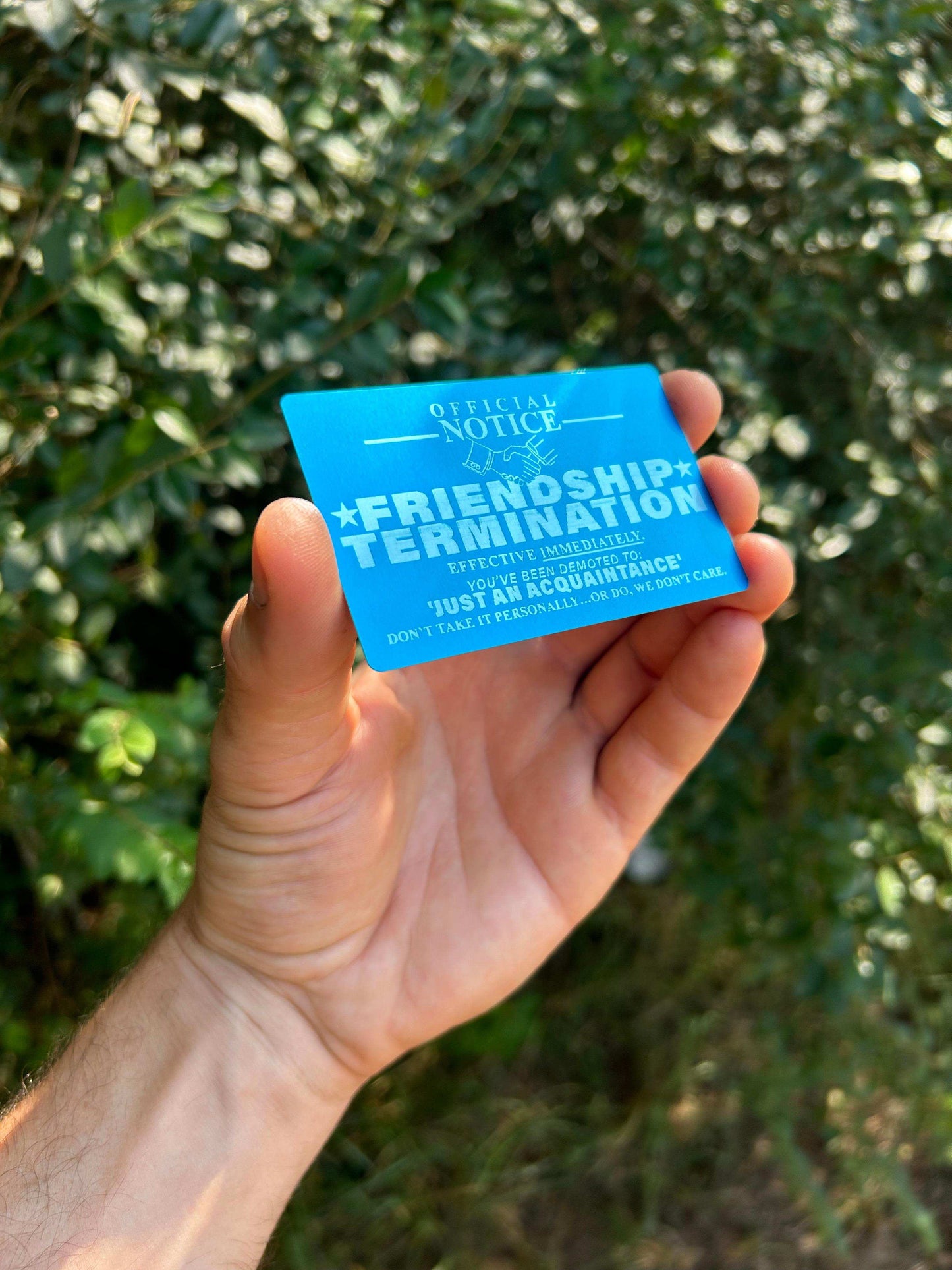 laser engraved friendship termination gag gift card product demonstration, blue/silver color metal keepsake in an outdoor setting