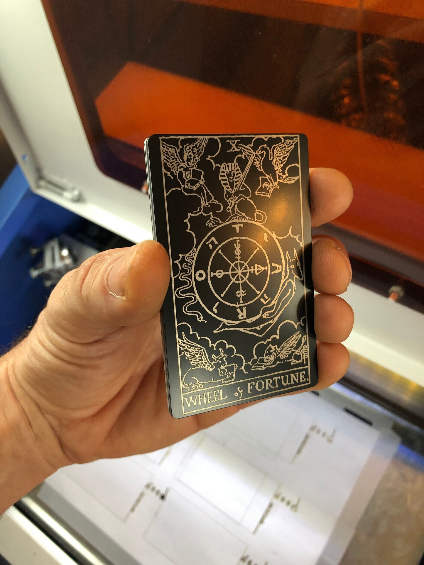 Hand holding a tarot card with 'Wheel of Fortune' design against a blurred indoor background