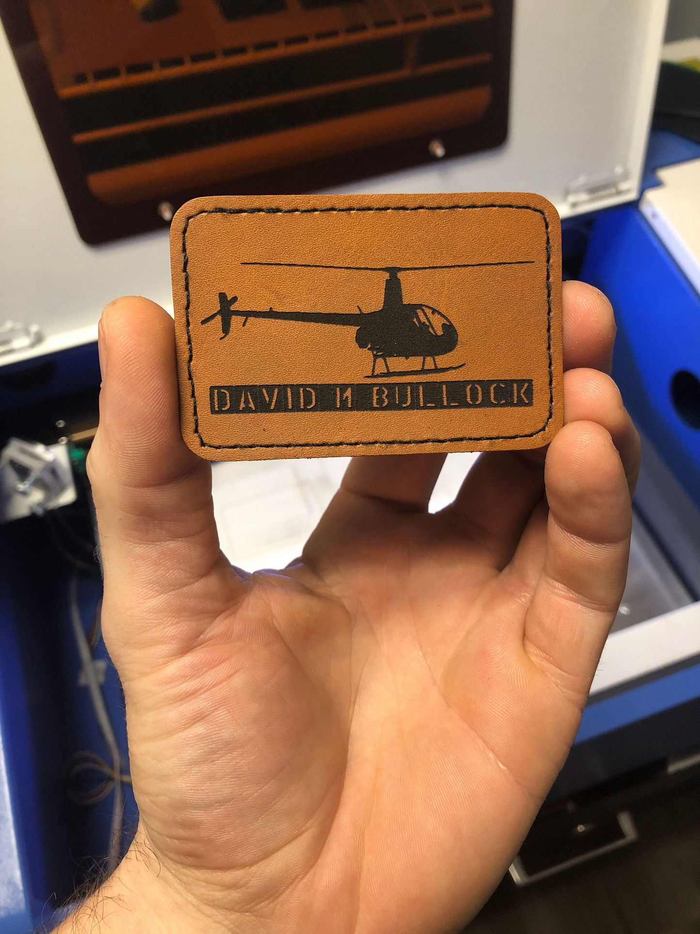 Hand holding a brown leather patch with helicopter design and custom name text flight patch.