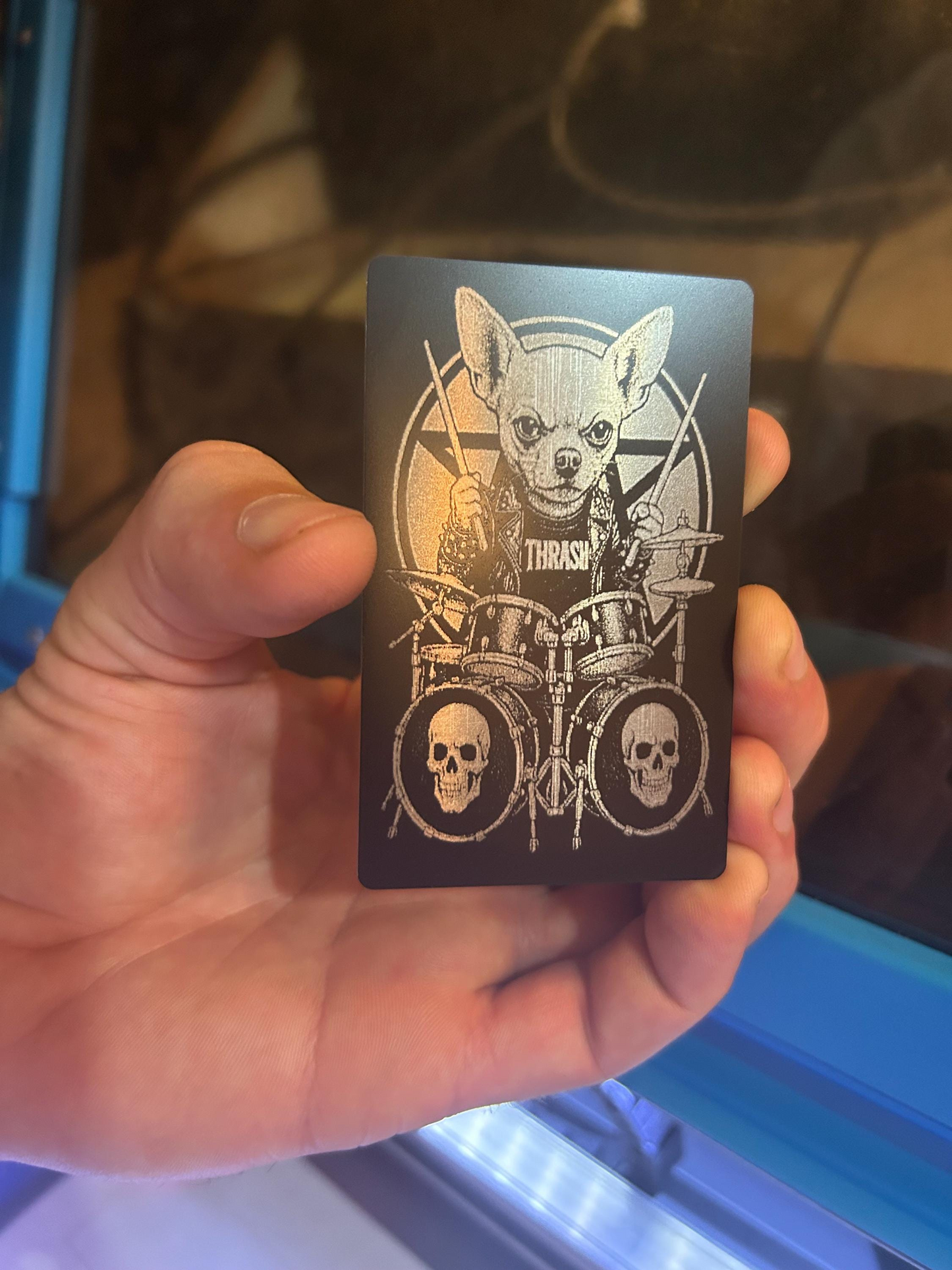 Hand holding a black metal novelty keepsake card with a graphic design of a chihuahua and double bass drum set