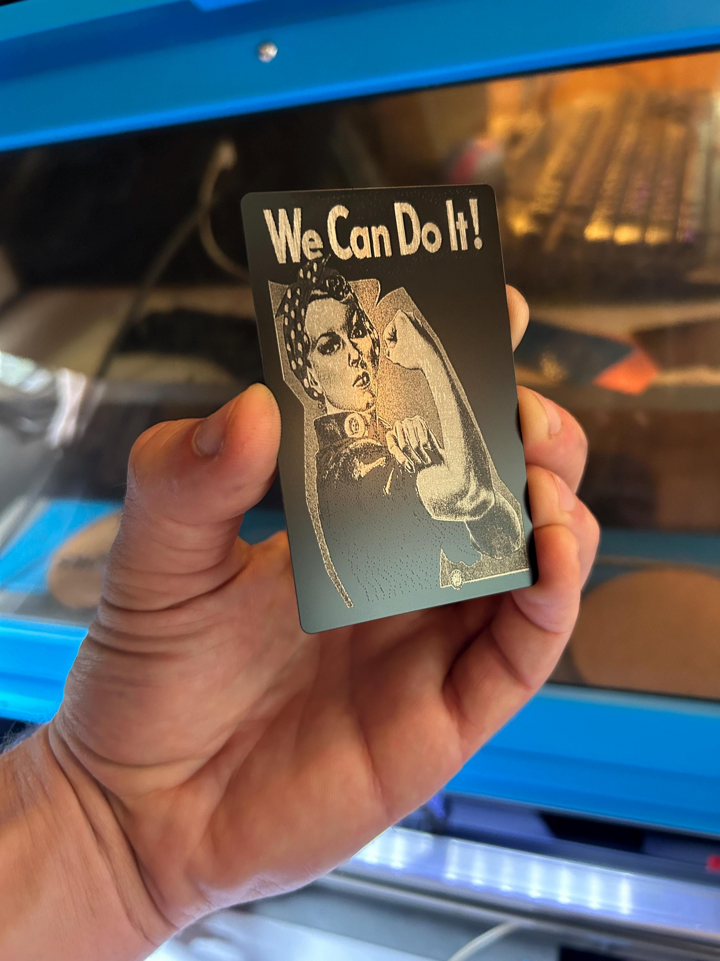 Hand holding a metal gift card with 'We Can Do It!' text and a vintage-style illustration.