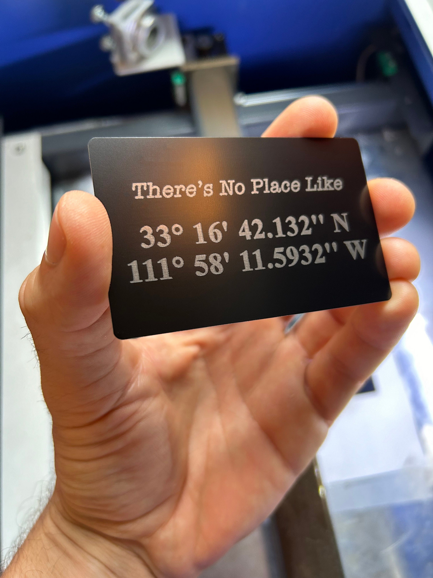 Hand holding a metal black/silver personalized gift card with coordinates and customized text example