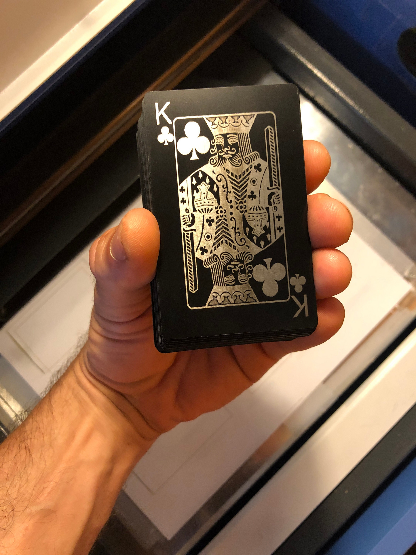 Hand holding a deck of metal black/silver playing cards, with King of Clubs on top