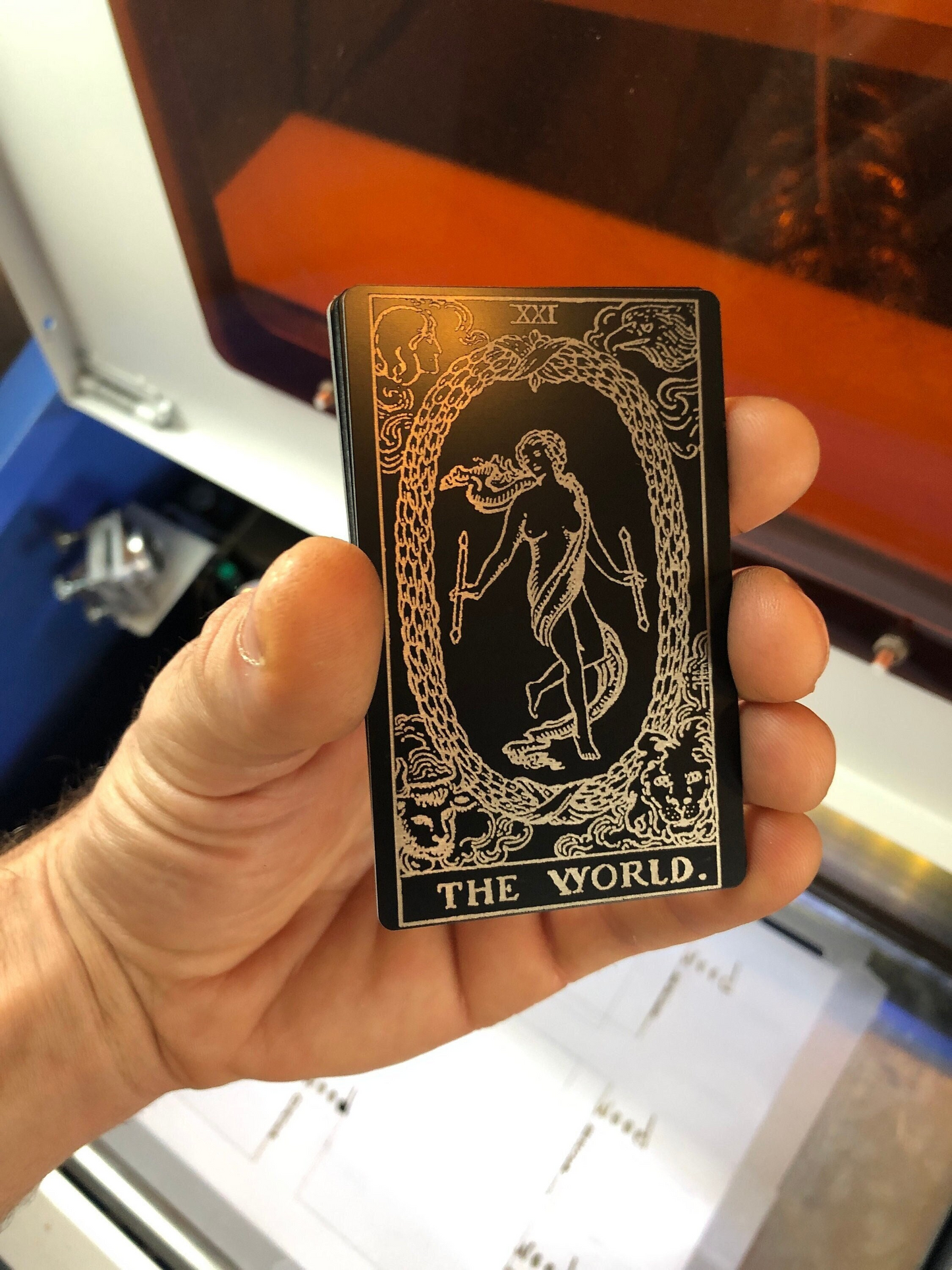 Hand holding a black and silver metal tarot wallet card with 'The World' symbol laser engraved