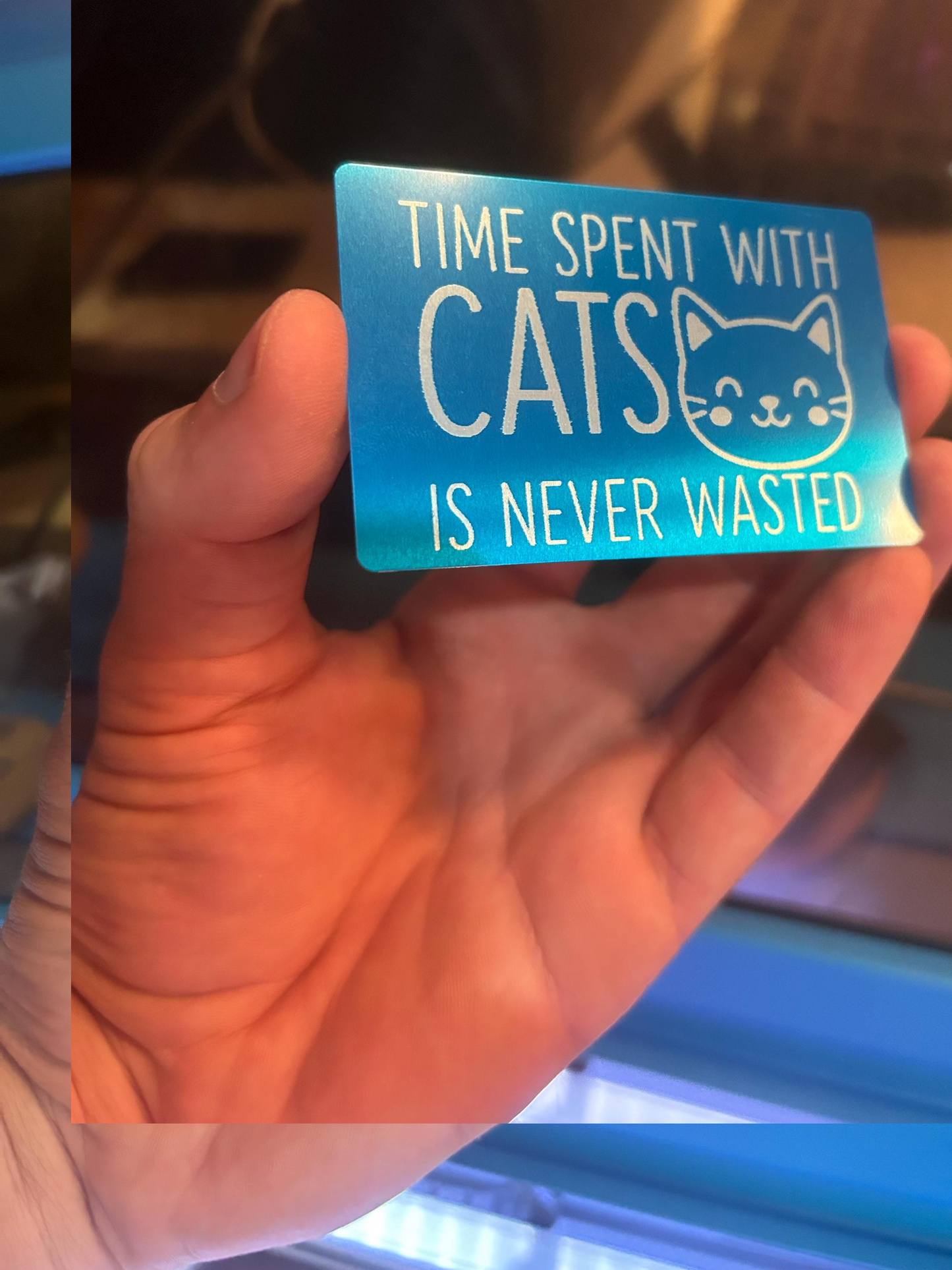 Detailed shot of blue and silver anodized aluminum cat keepsake card engraved with kitten art and cat lover quote