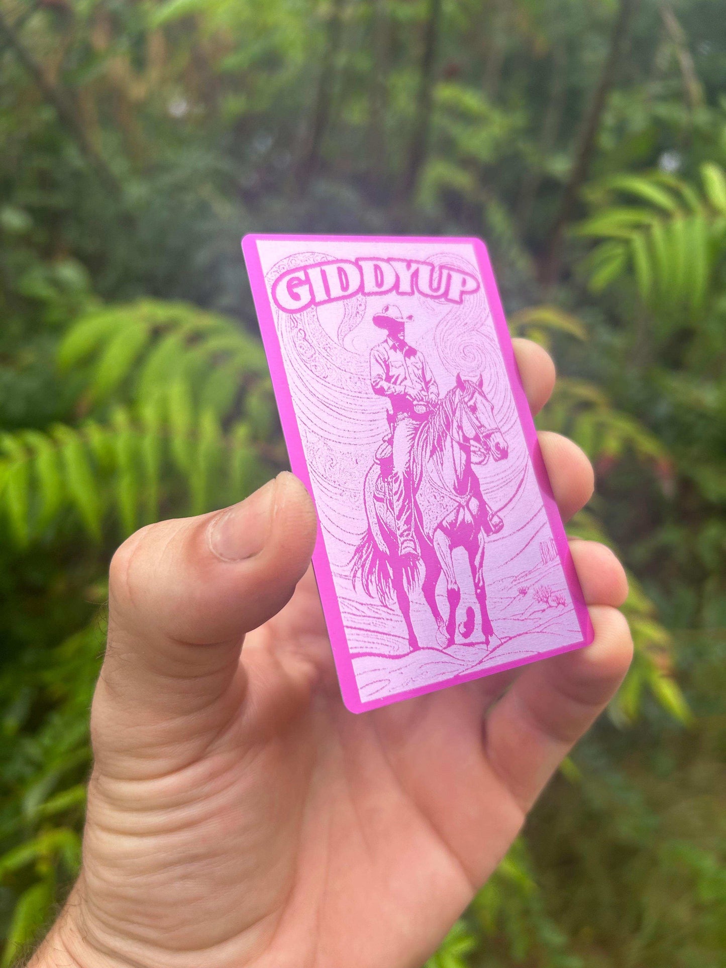 Hand holding a purple 'Giddy Up' card with a horse illustration against a blurred green background