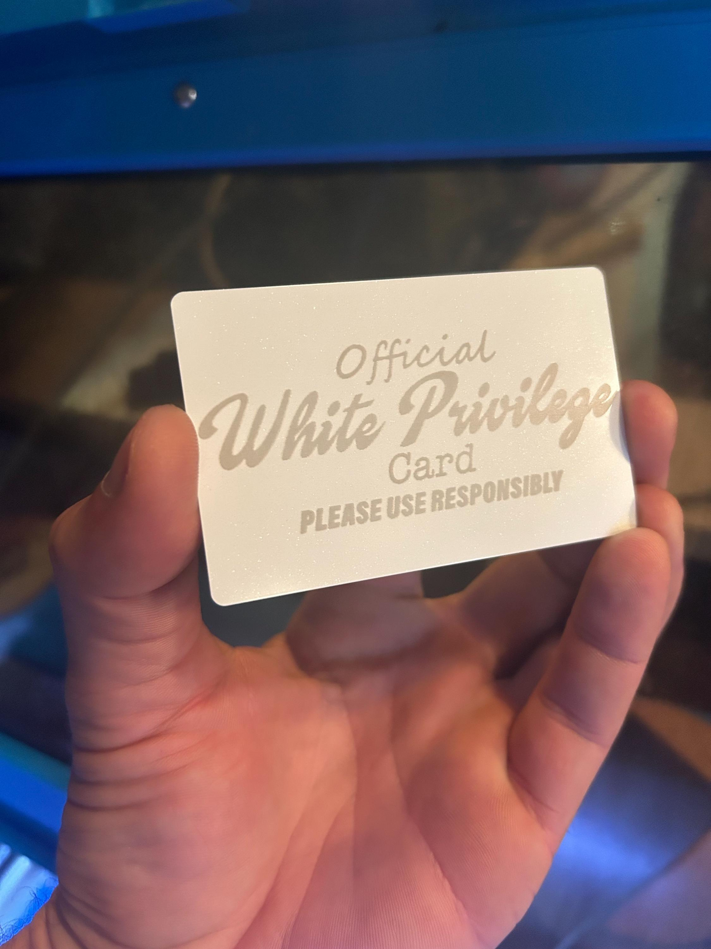 Hand holding a metal gift card with 'Official White Privilege Card' novelty political text.