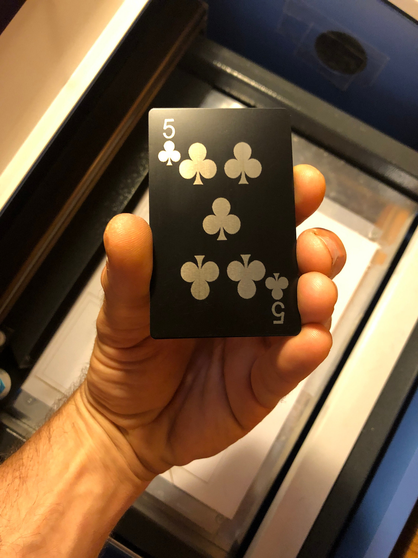 Hand holding a black metal gaming playing card with five of clubs design laser engraved