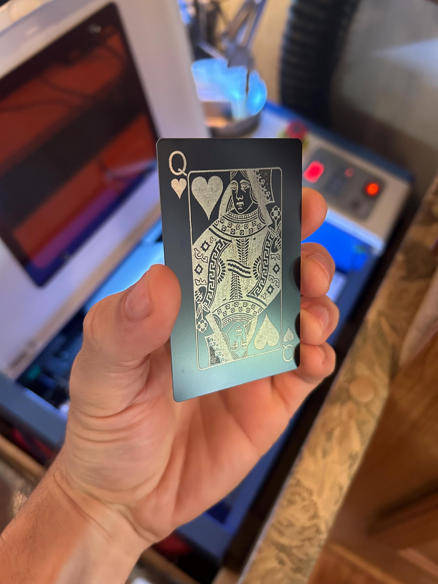 Hand holding a playing card with a queen of hearts design in front of a machine.