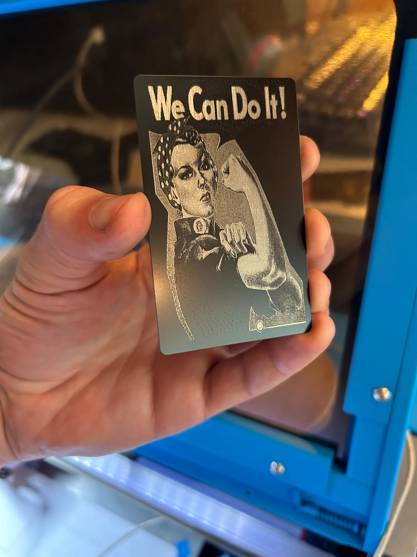 Hand holding a laser engraved novelty wallet card of rosie the riveter flexing with We can do it classic wwII poster engraving art