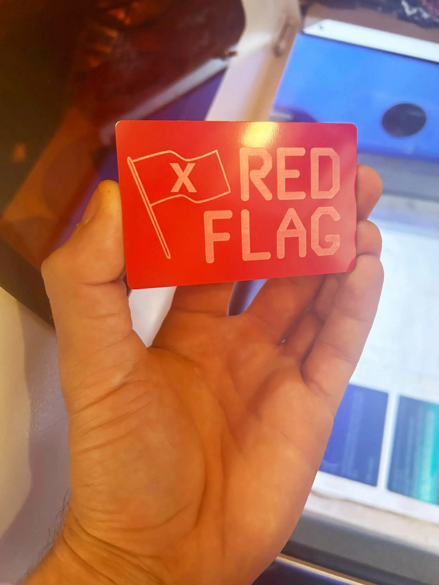 Hand holding a laser engraved novelty red card with 'X RED FLAG' text and flag symbol.