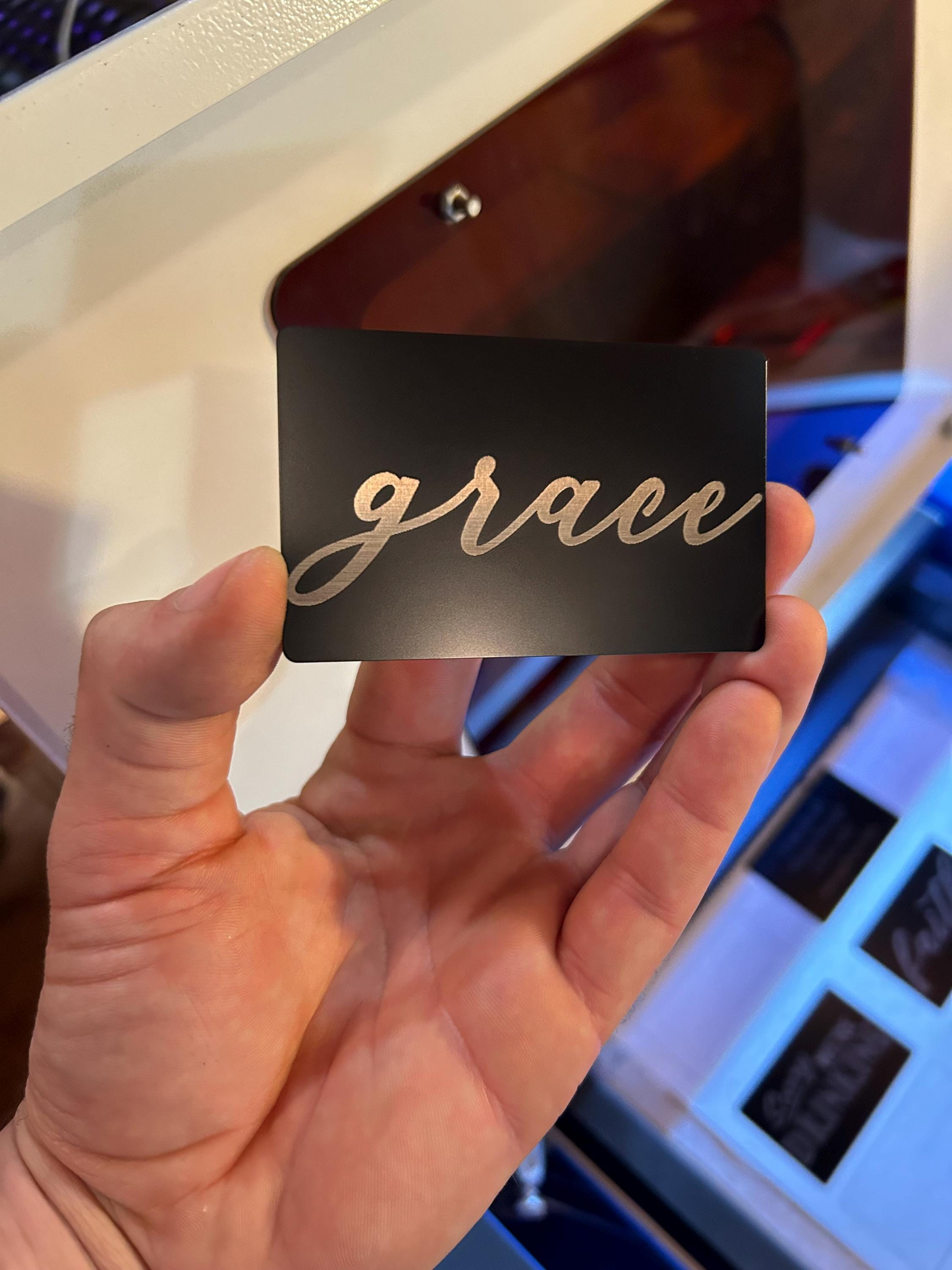 Hand holding a black card with faith inspired 'grace' text engraved in silver cursive on a blurred background