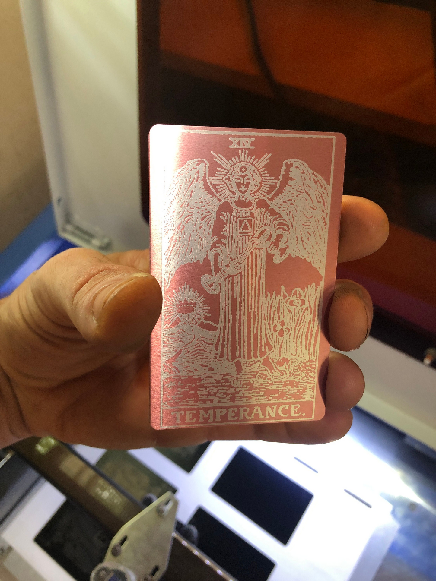 Keepsake Anodized Aluminum laser engraved gift tarot card with 'Temperance' design held by a hand in front of a blurred background
