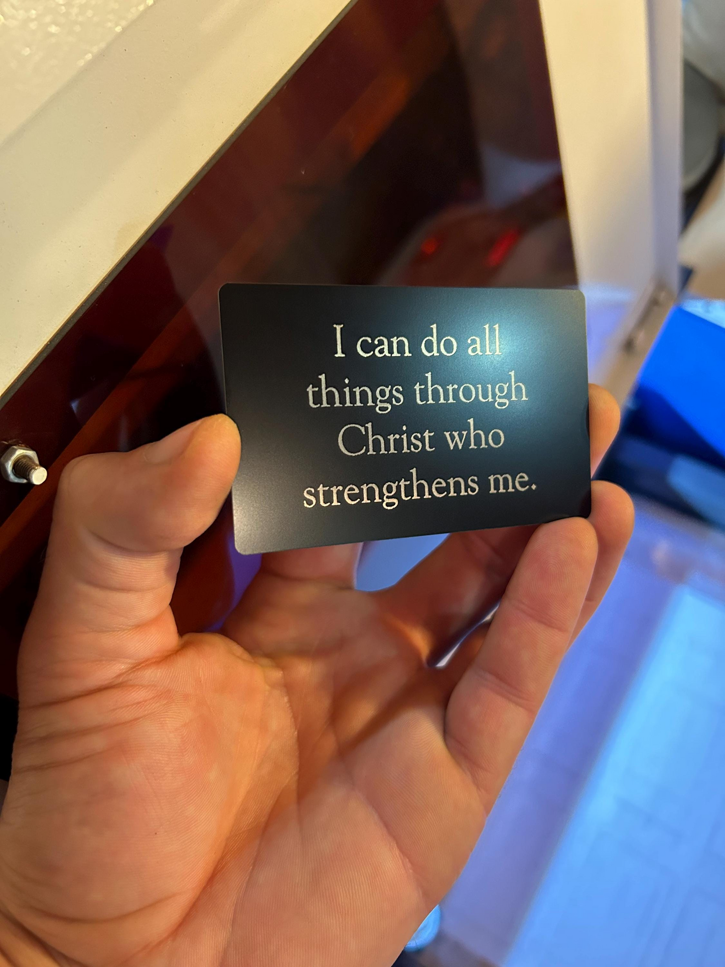 Hand holding a metal scripture prayer card with a motivational bible quote in front of a blurred background