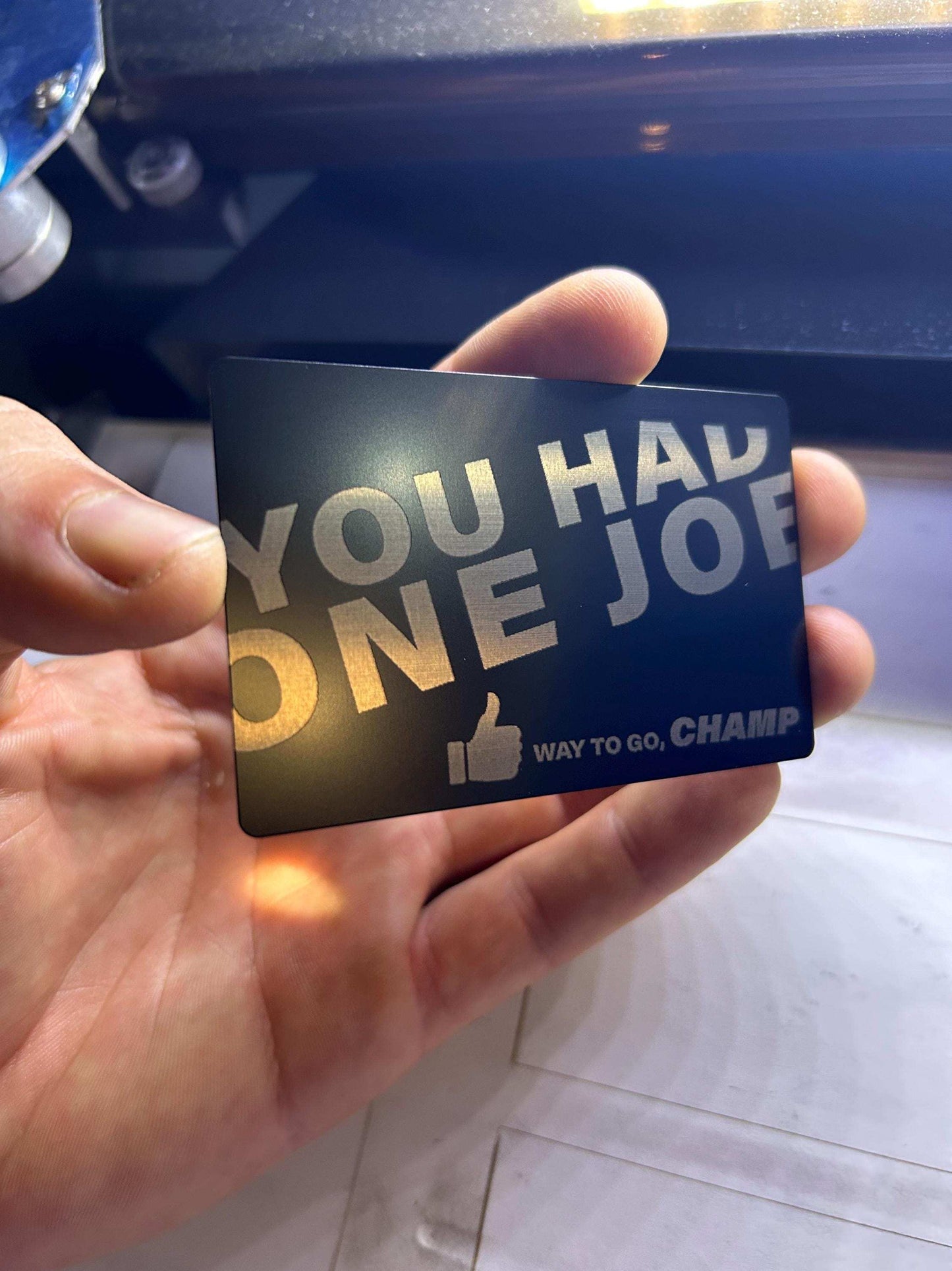 Hand holding a card with 'You had one job' text in front of a laser machine interior.