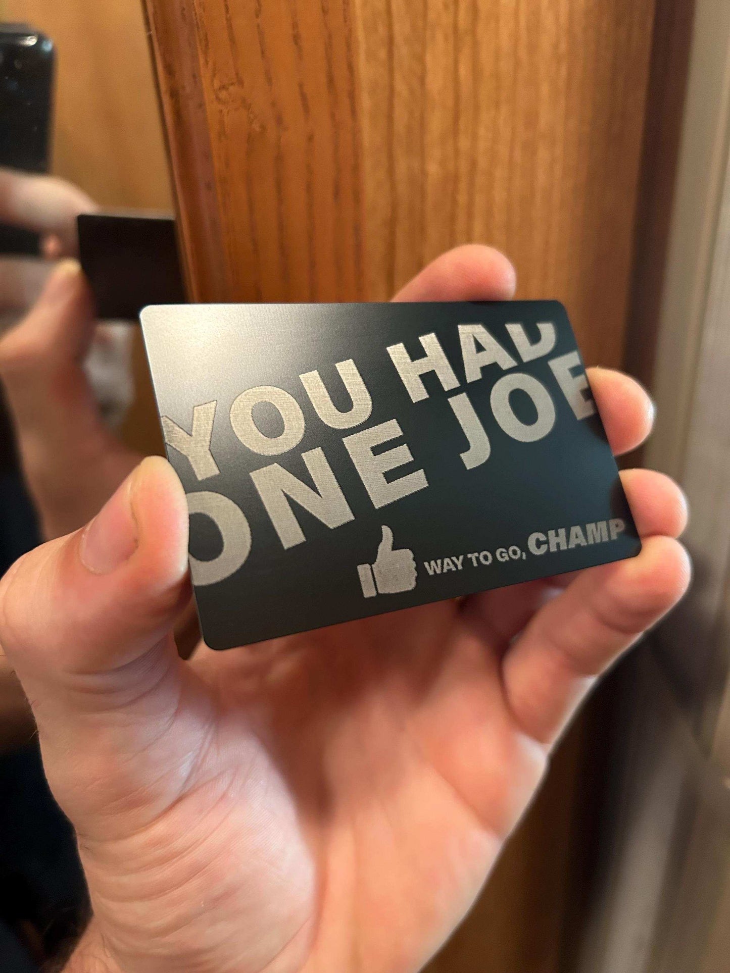 Hand holding a metal greeting card with text 'YOU HAD ONE JOE' and a thumbs-up icon.
