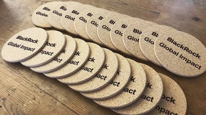 Set of cork coasters with 'BlackRock Global Impact' branding on a wooden surface