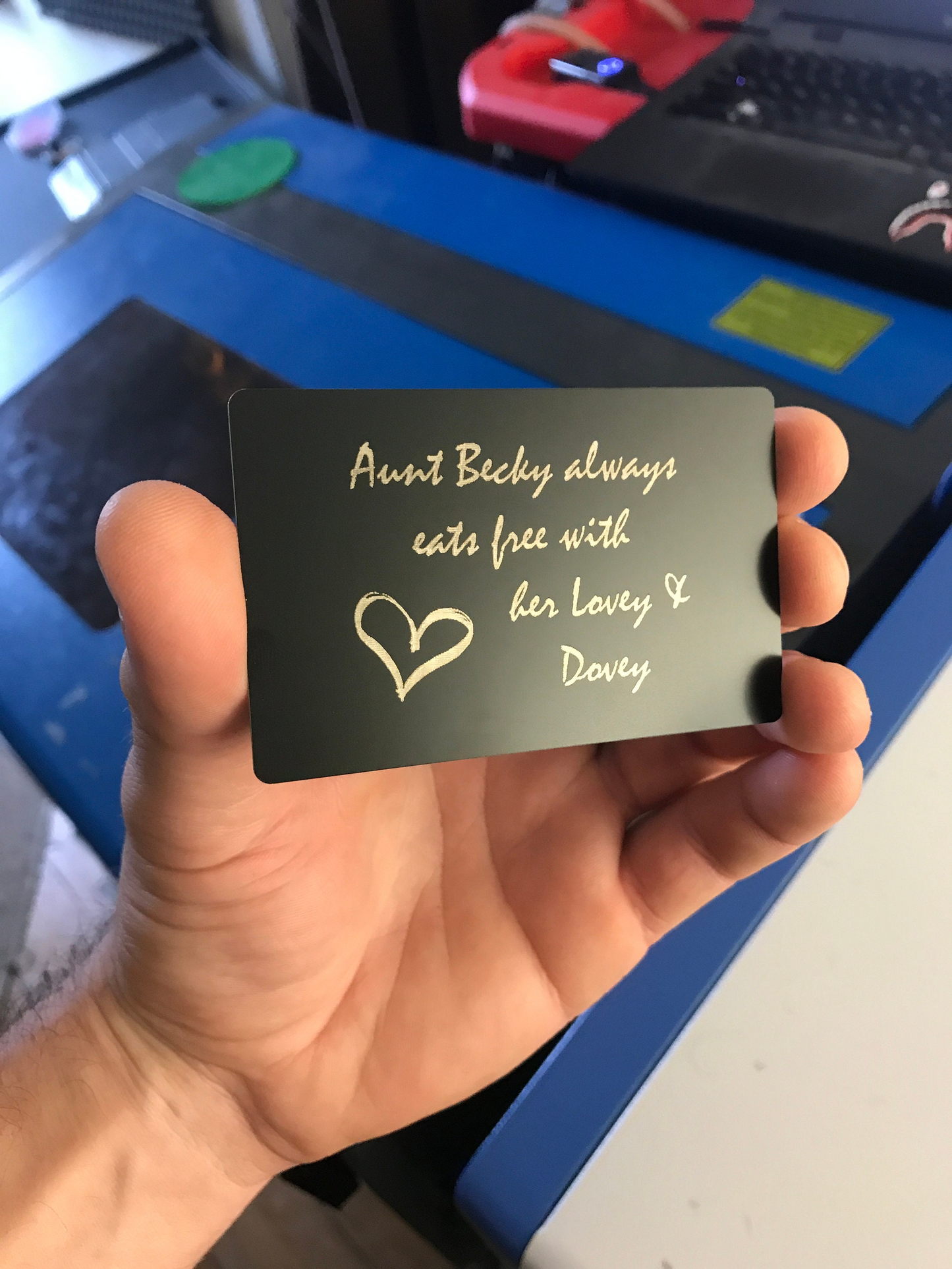 Hand holding a black custom metal keepsake card with personalized text engraving and a heart symbol.
