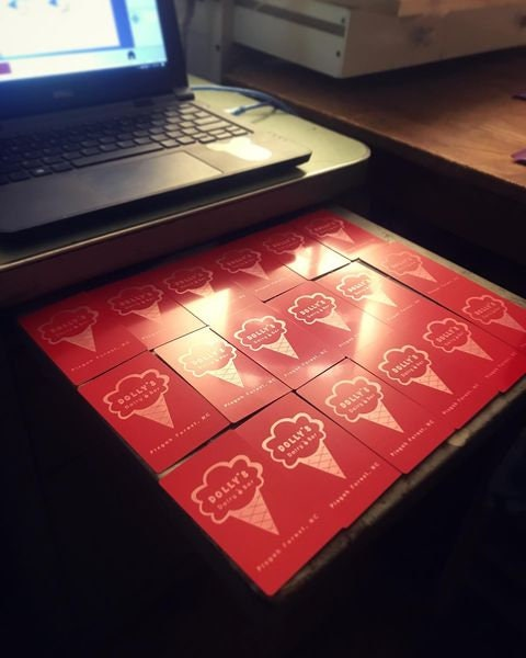 Set of red/silver laser engraved metal business cards with ice cream shop cone logo and text design on a desk next to a laptop